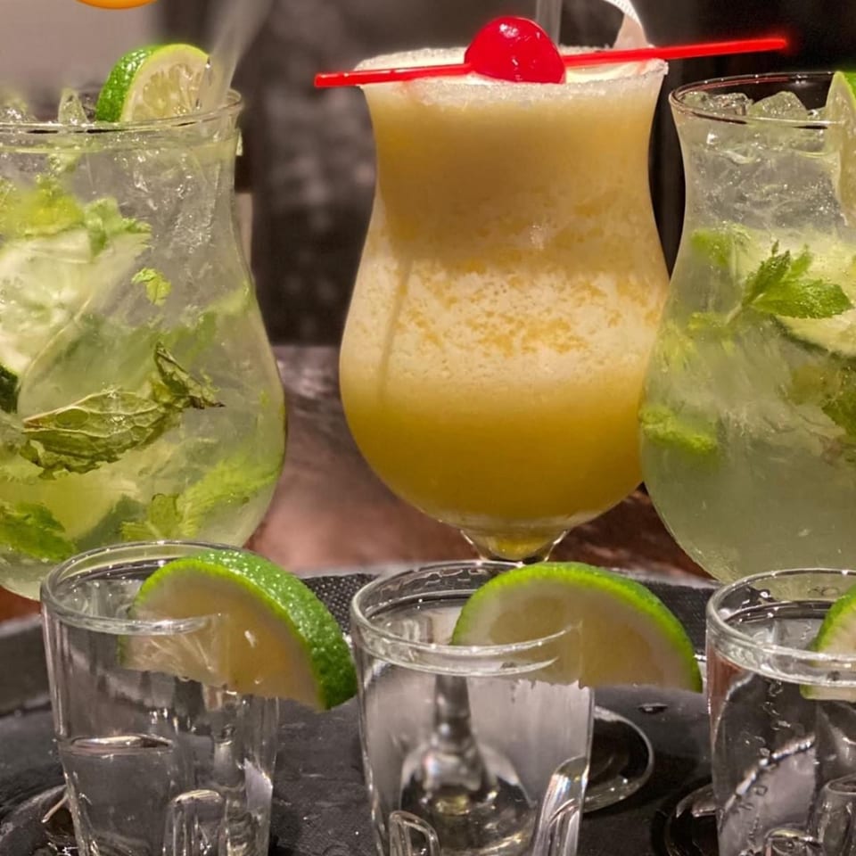 Three cocktails, two mojitos with lime and mint, and one frozen drink with a cherry and red straw.