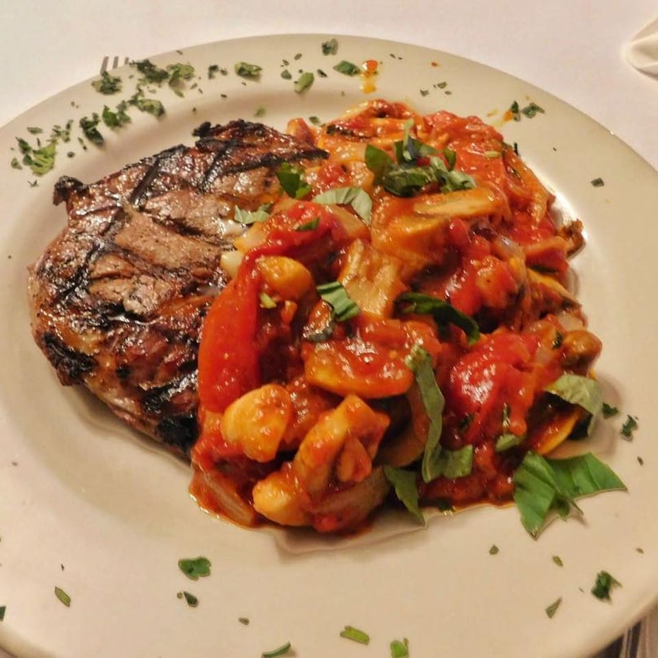 Grilled steak with a side of gnocchi in a rich tomato sauce, garnished with fresh basil.