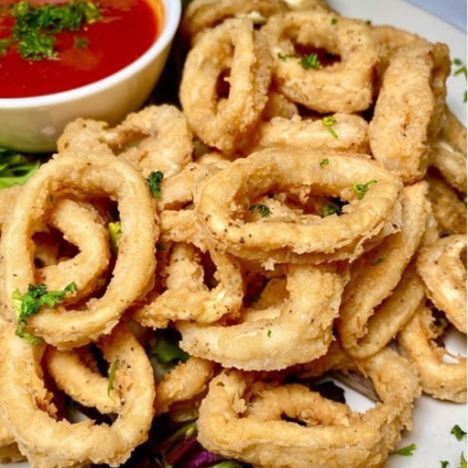 Crispy fried calamari rings with a side of red marinara sauce, garnished with parsley.